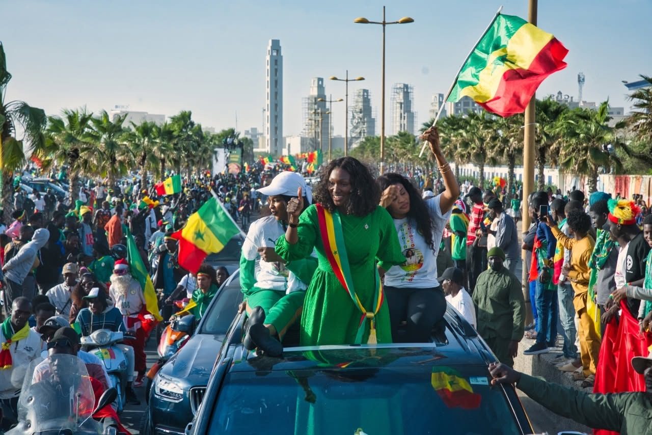Grande caravane — la Présidente en vert, écharpe tricolore, parmi une marée de drapeaux